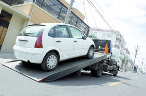 A small white car is being loaded onto a flatbed tow truck from Fairfax Tow Truck